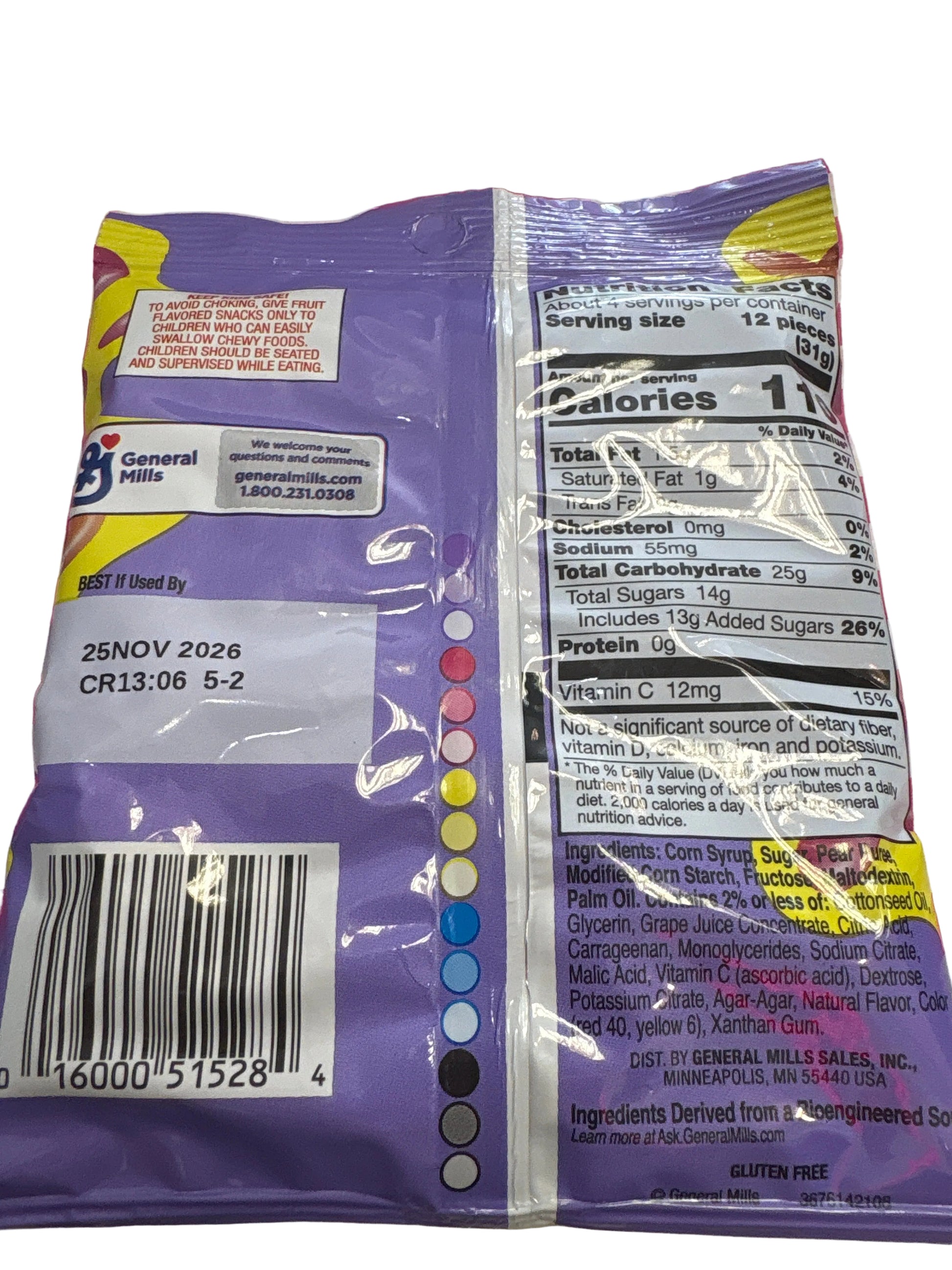 The back of a General Mills candy bag, showing the nutrition facts panel, barcode, and a vertical color wheel indicating product colors, laid on a pink and white striped fabric surface.